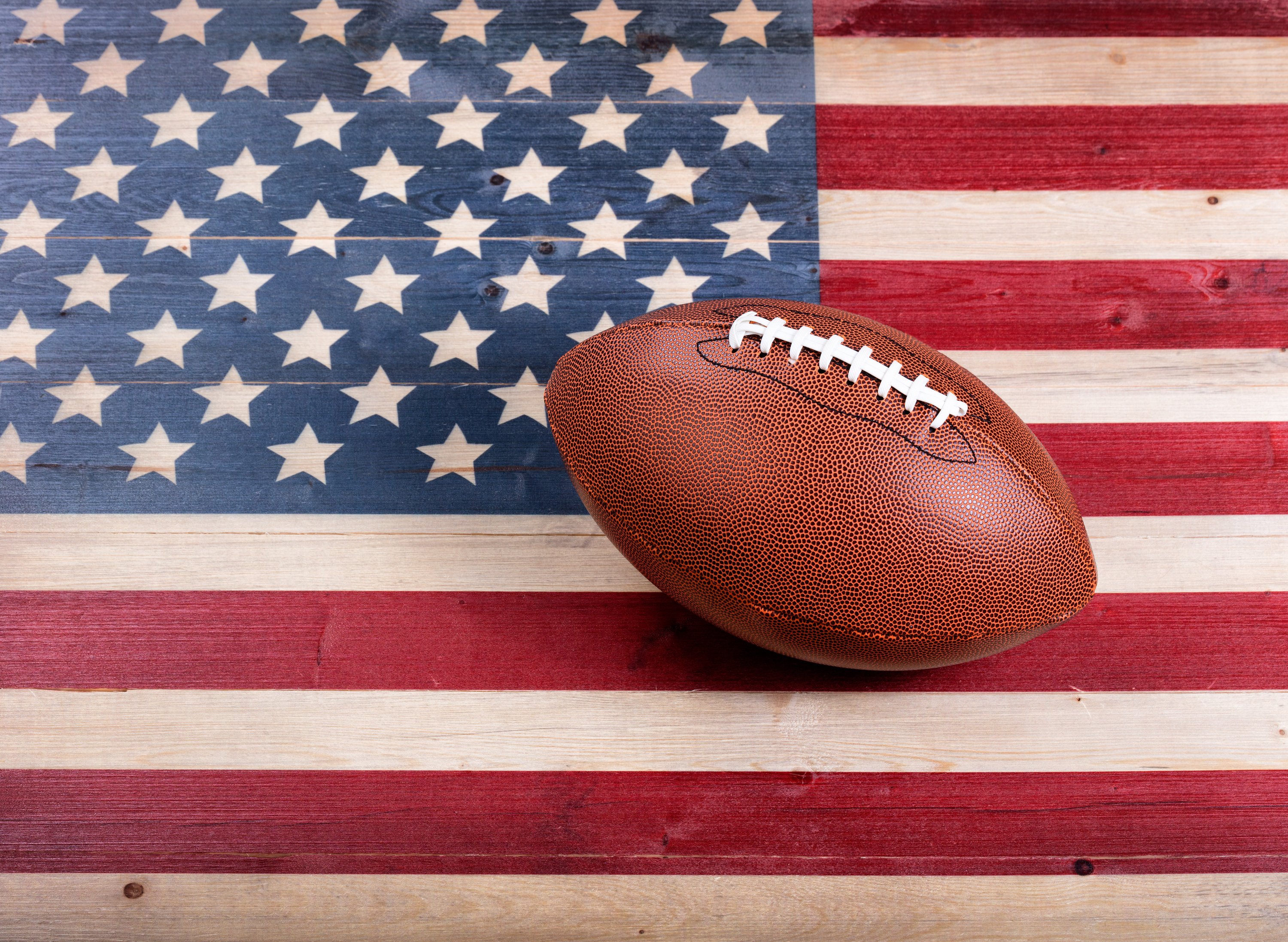 Top view of American football on rustic wooden boards with painted USA Flag.